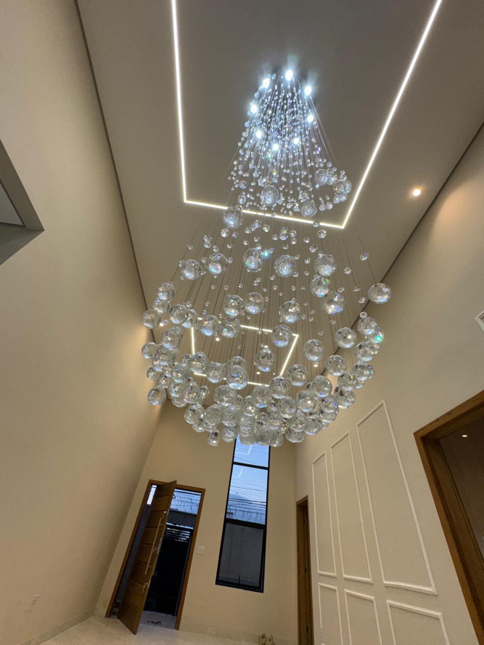 Lustre de cristal com a porta de entrada iluminada ao fundo